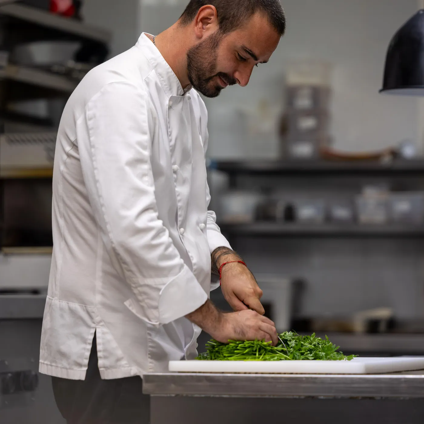 A man in a white jacket prepares herbs on a worktop in a professional kitchen.