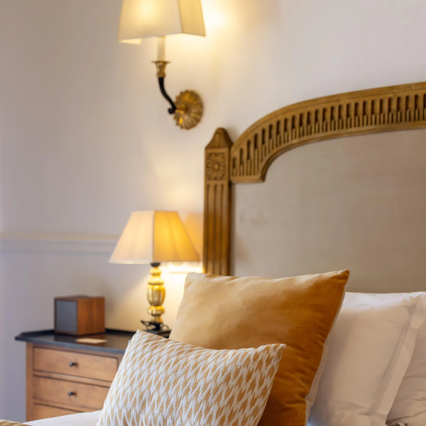 Bed with a wooden headboard, cushions, and a lit lamp turned on