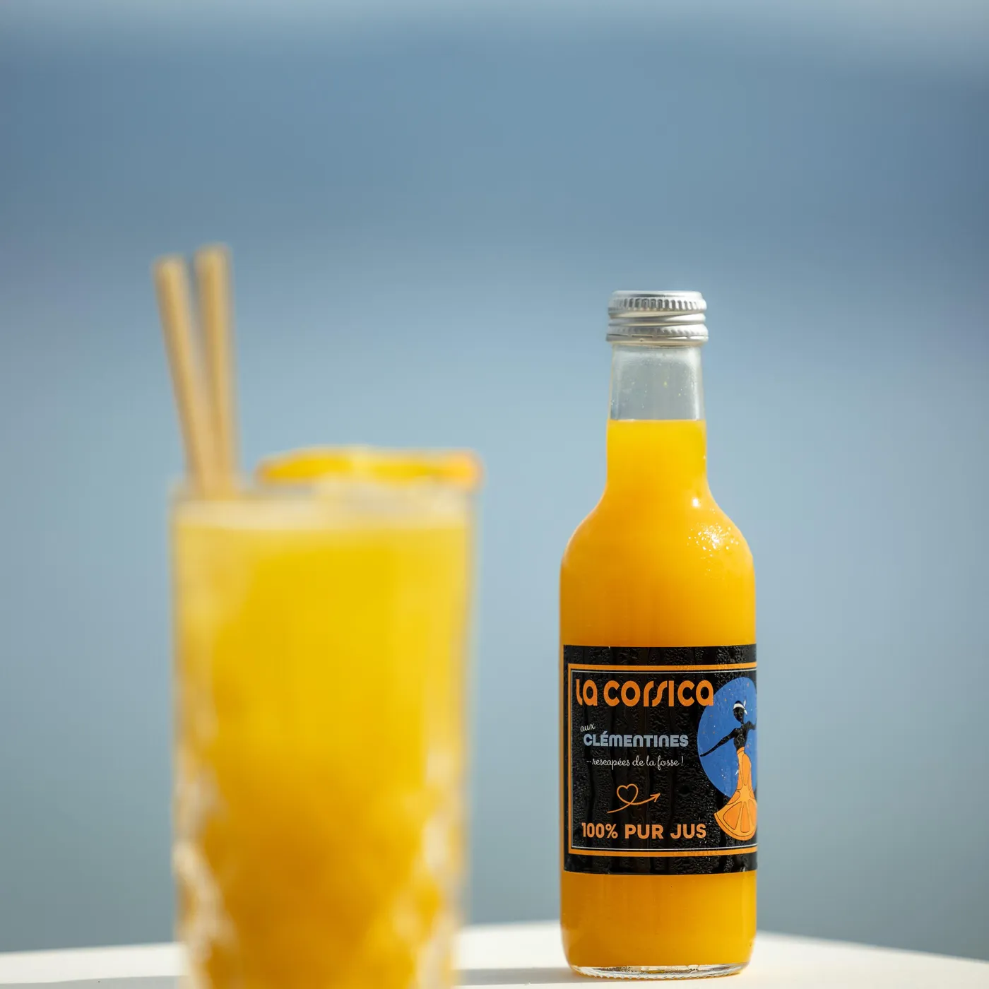 Bottle of clementine juice next to a glass containing the same juice with straws