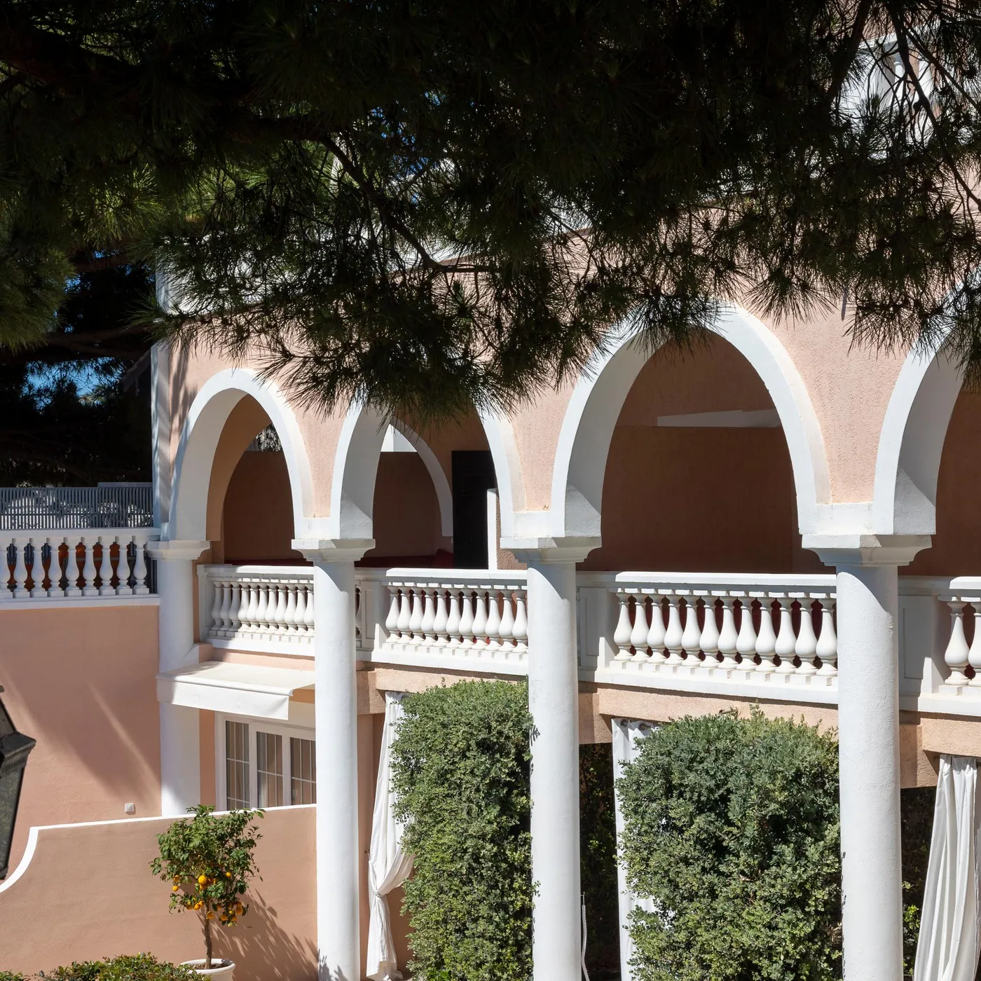 Balcon avec arches et balustrade blanche, entouré d'arbres et de végétation, avec une lanterne noire suspendue