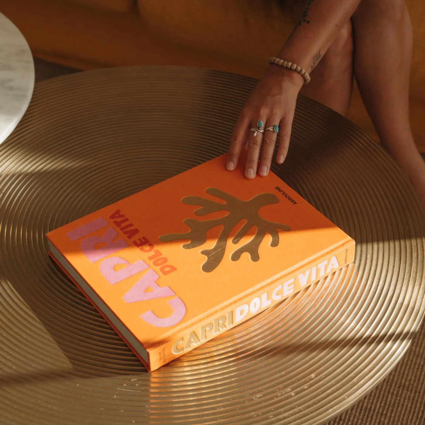 A hand places an orange book on a metal plate set on a striated surface.
