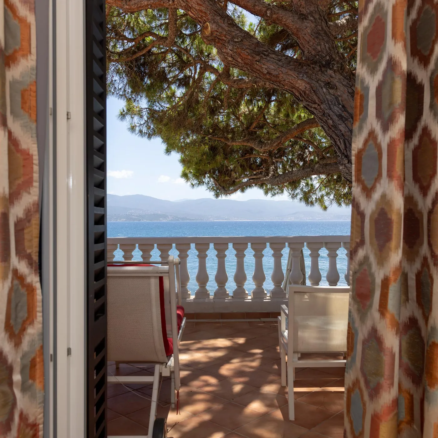 Balcon with sea view, colorful patterned curtains and wicker chairs