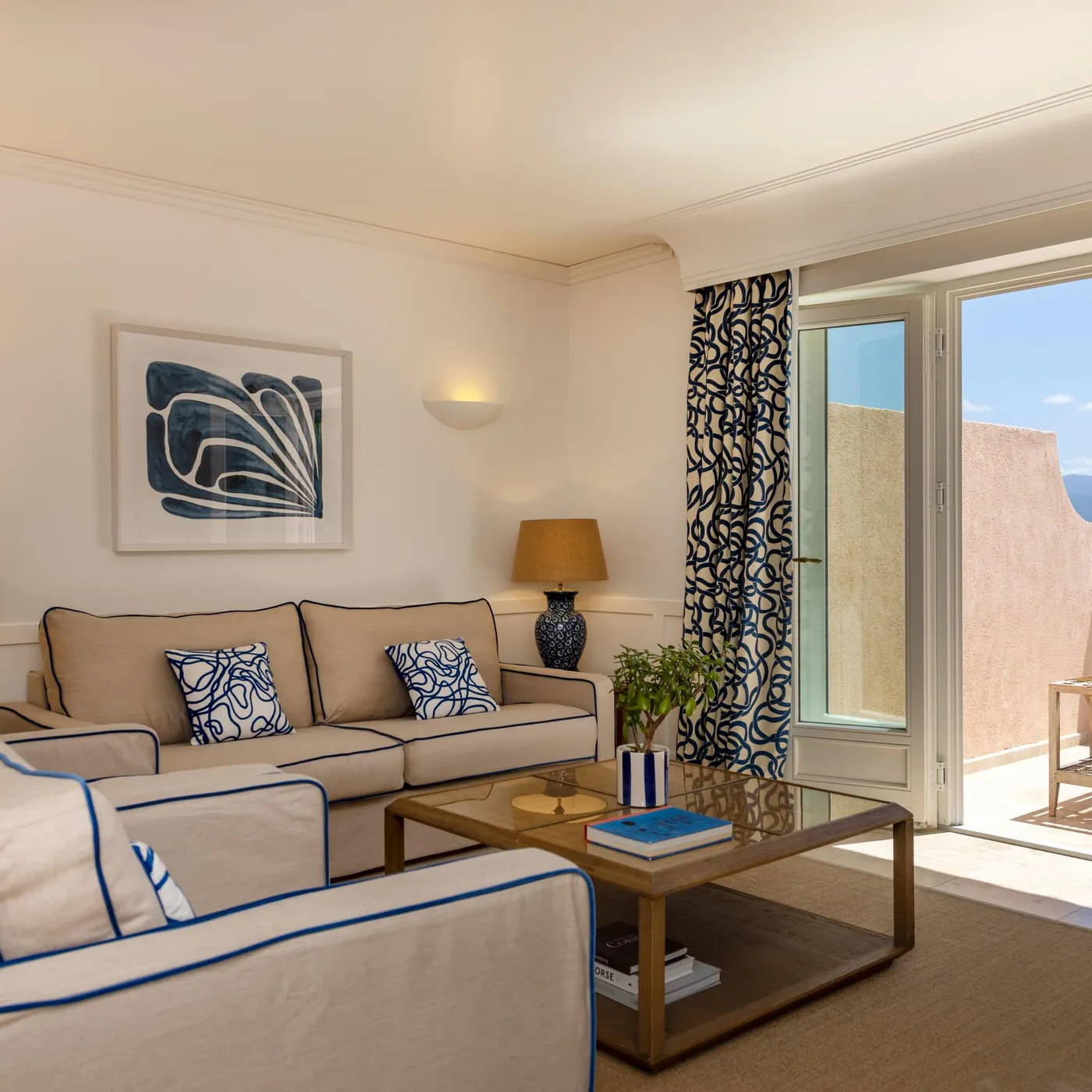 Living room with beige sofa with blue borders, glass coffee table, sea view through an open French door