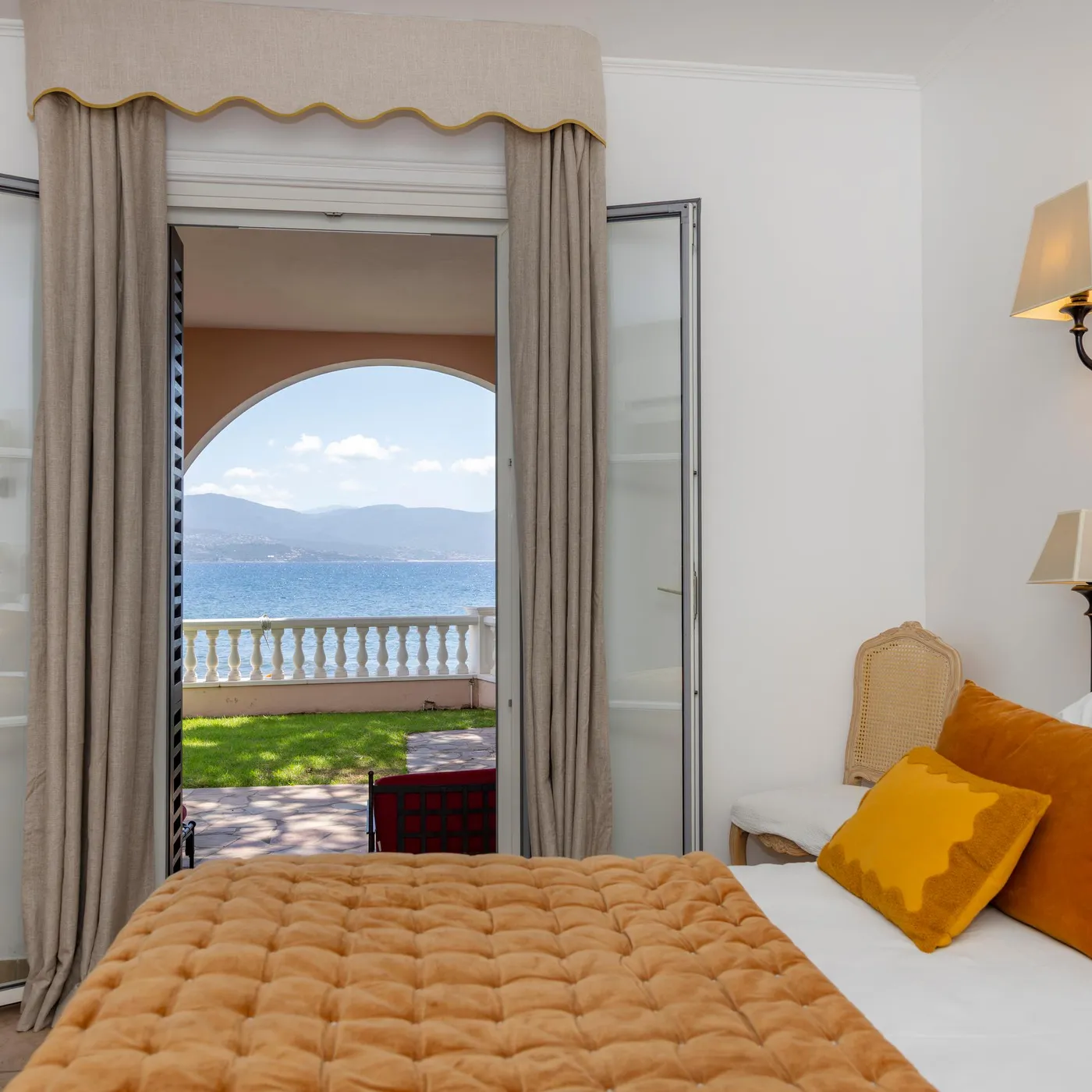 Room with wooden headboard bed and view of a balcony overlooking a lake and mountains