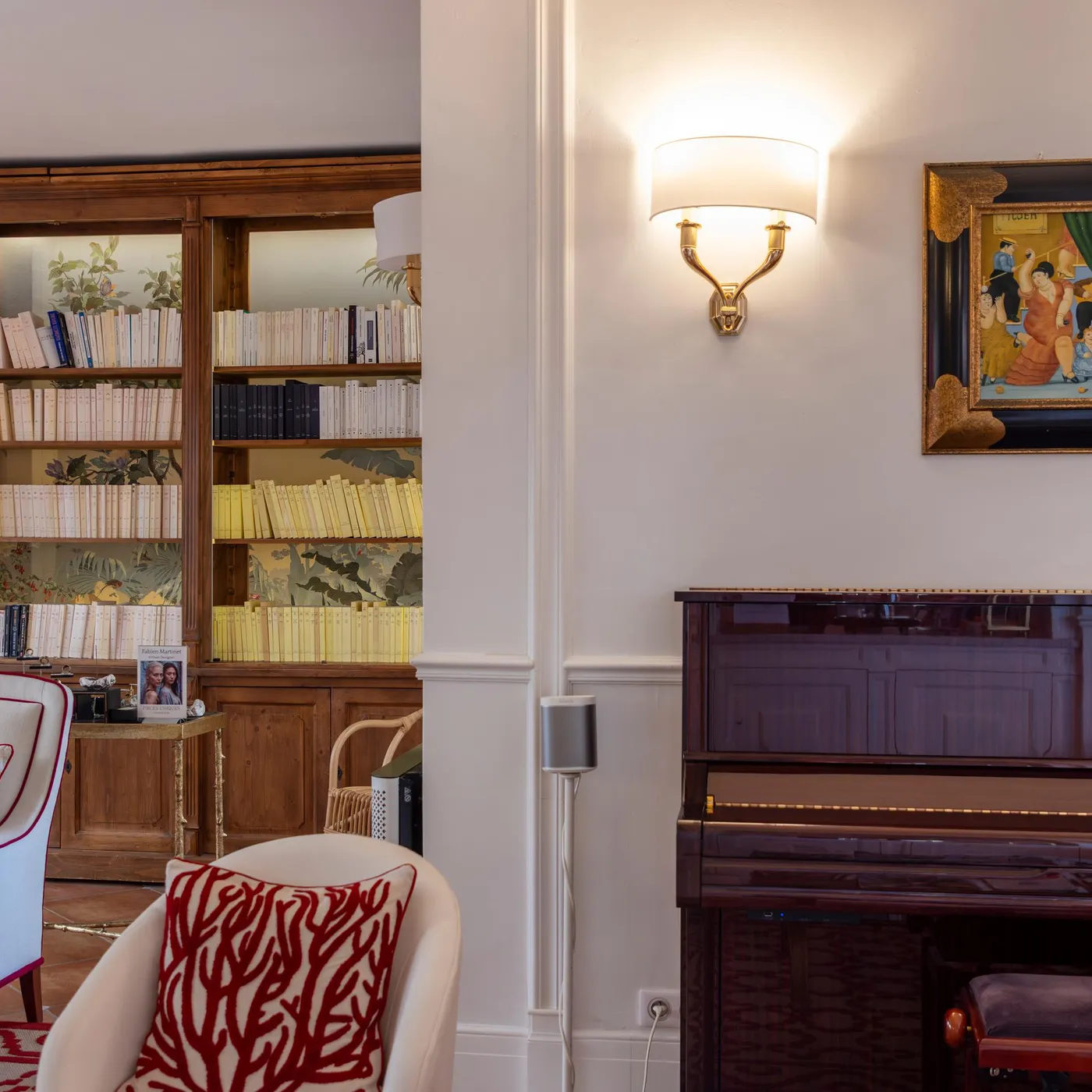 A living room with shelves filled with books, armchairs, a painting, and lit wall sconces.