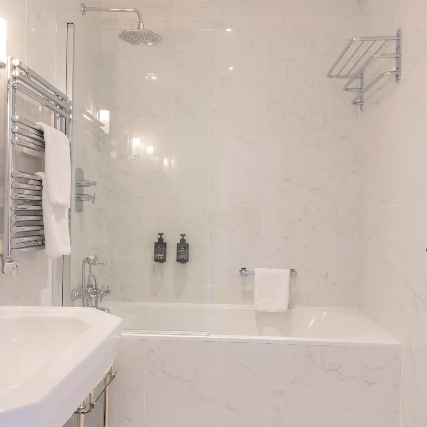 Bathroom with bathtub, rain shower, sink, towels, and black and white tiled floor.