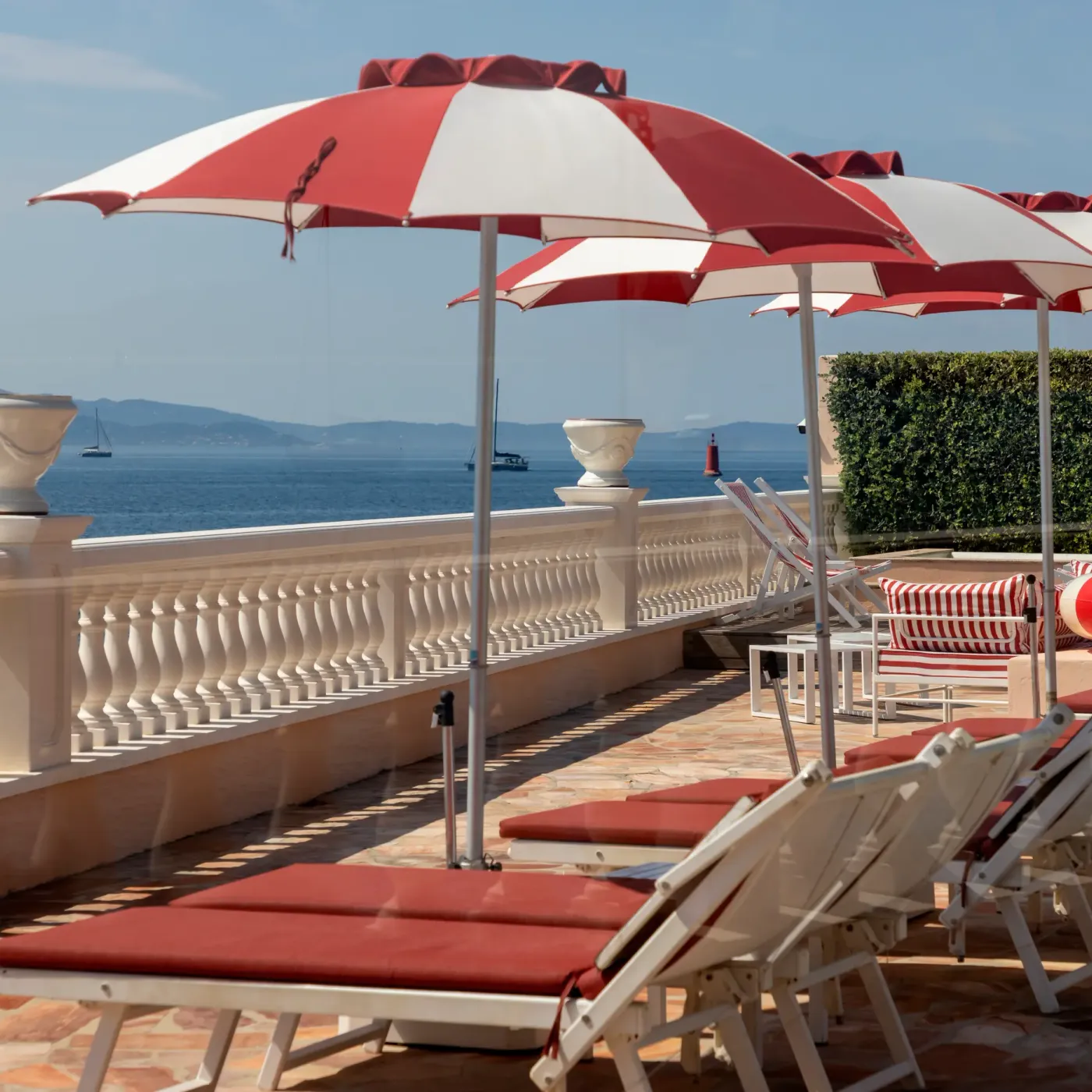 Une terrasse avec des transats, des parasols rayés rouges et blancs et une vue sur la mer