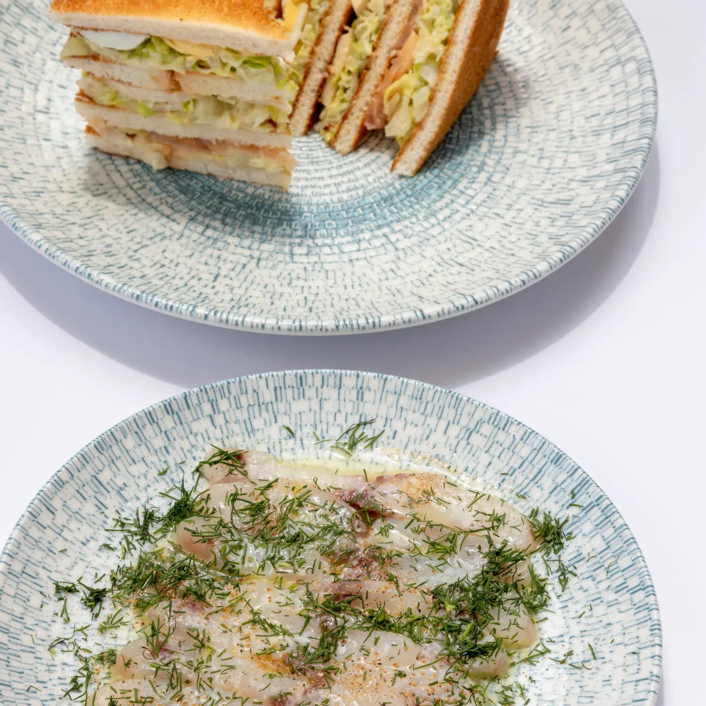 Two plates with cucumber and cream sandwiches and slices of toast topped with cucumber.