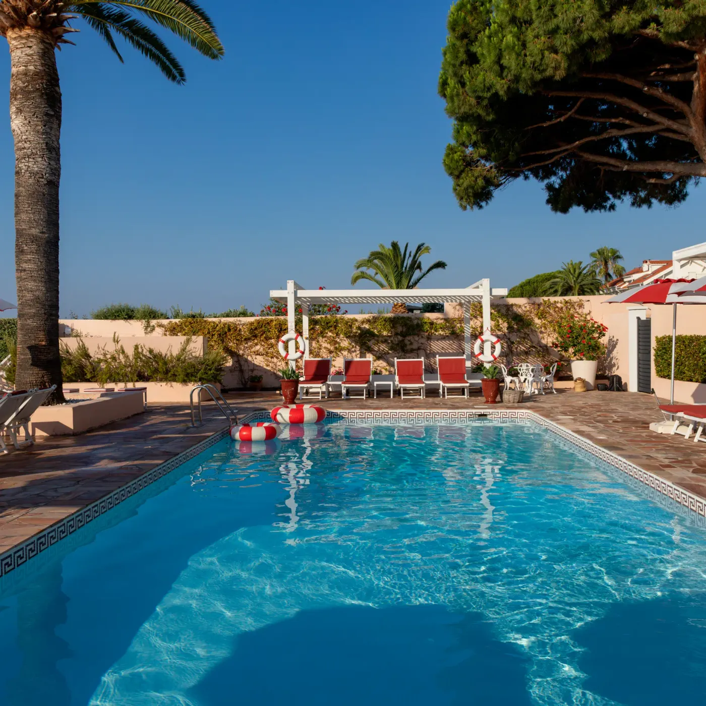 Piscine extérieure entourée de transats et de parasols, avec une vue sur la mer en arrière-plan