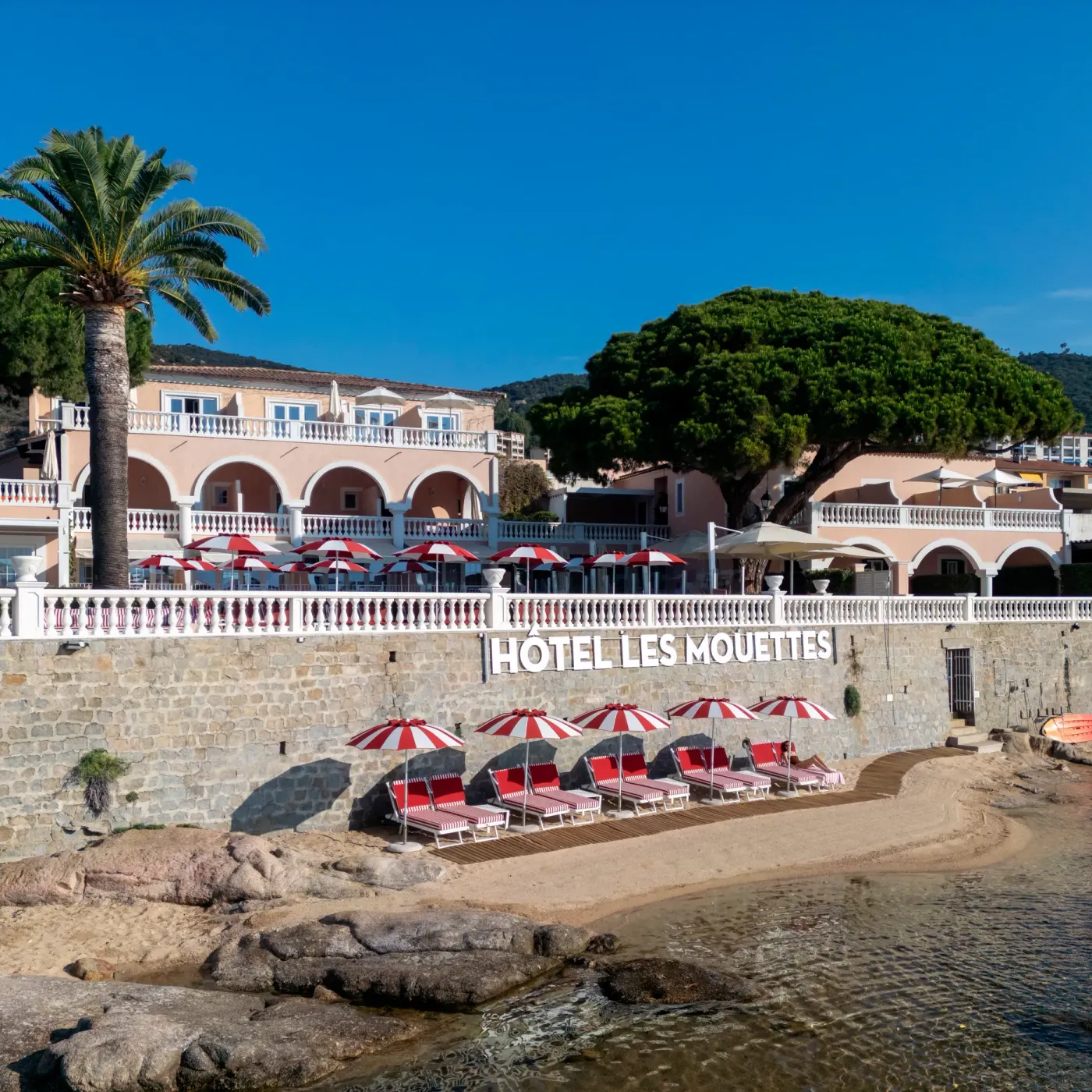Hôtel Les Mouettes avec une terrasse et des chaises longues en bord de mer sous des parasols rouges et blancs