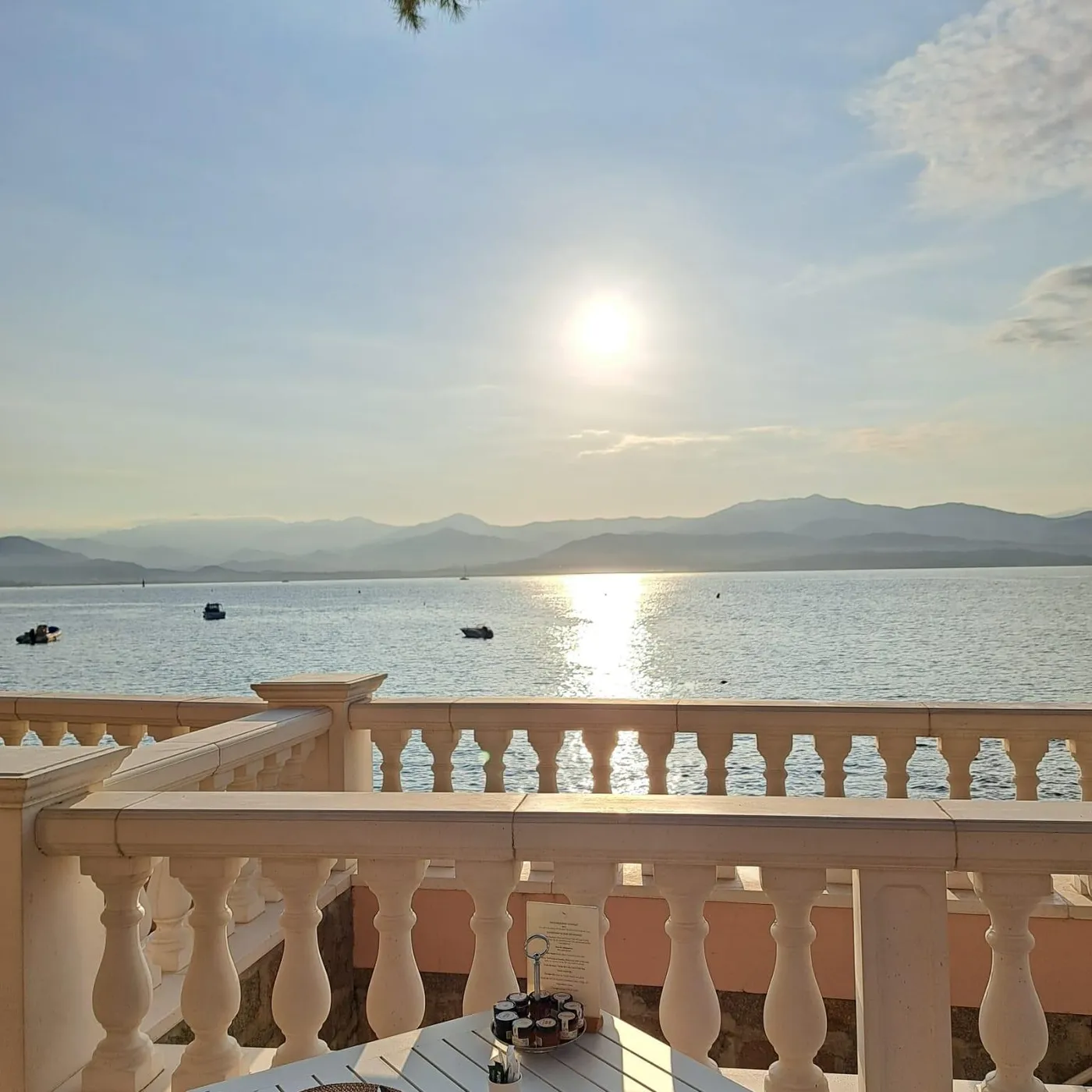 Table dressée avec couverts et serviettes sur une terrasse avec vue sur un lac et des montagnes au coucher du soleil