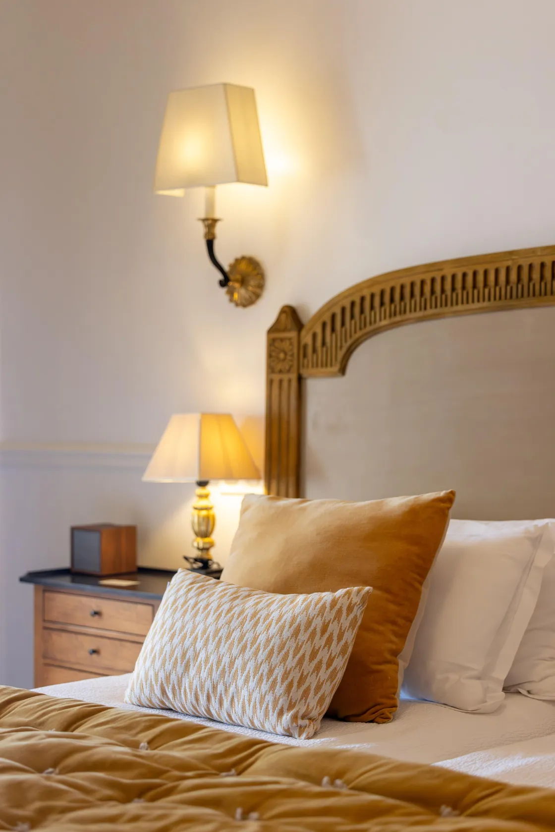 Bed met een houten bedkop met versieringen, kussens en een aangeschakelde nachtlamp