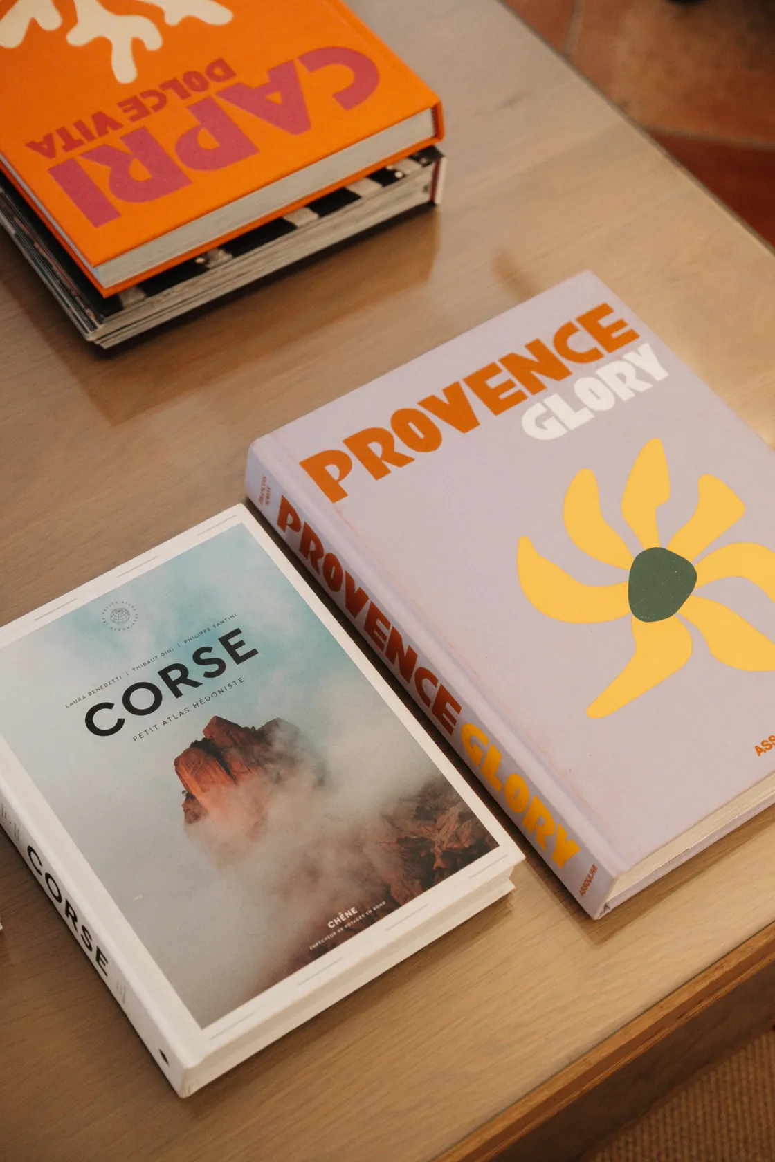 Drie boeken op een houten oppervlak, waarvan er één "Corse" en een ander "Provence Glory" heet