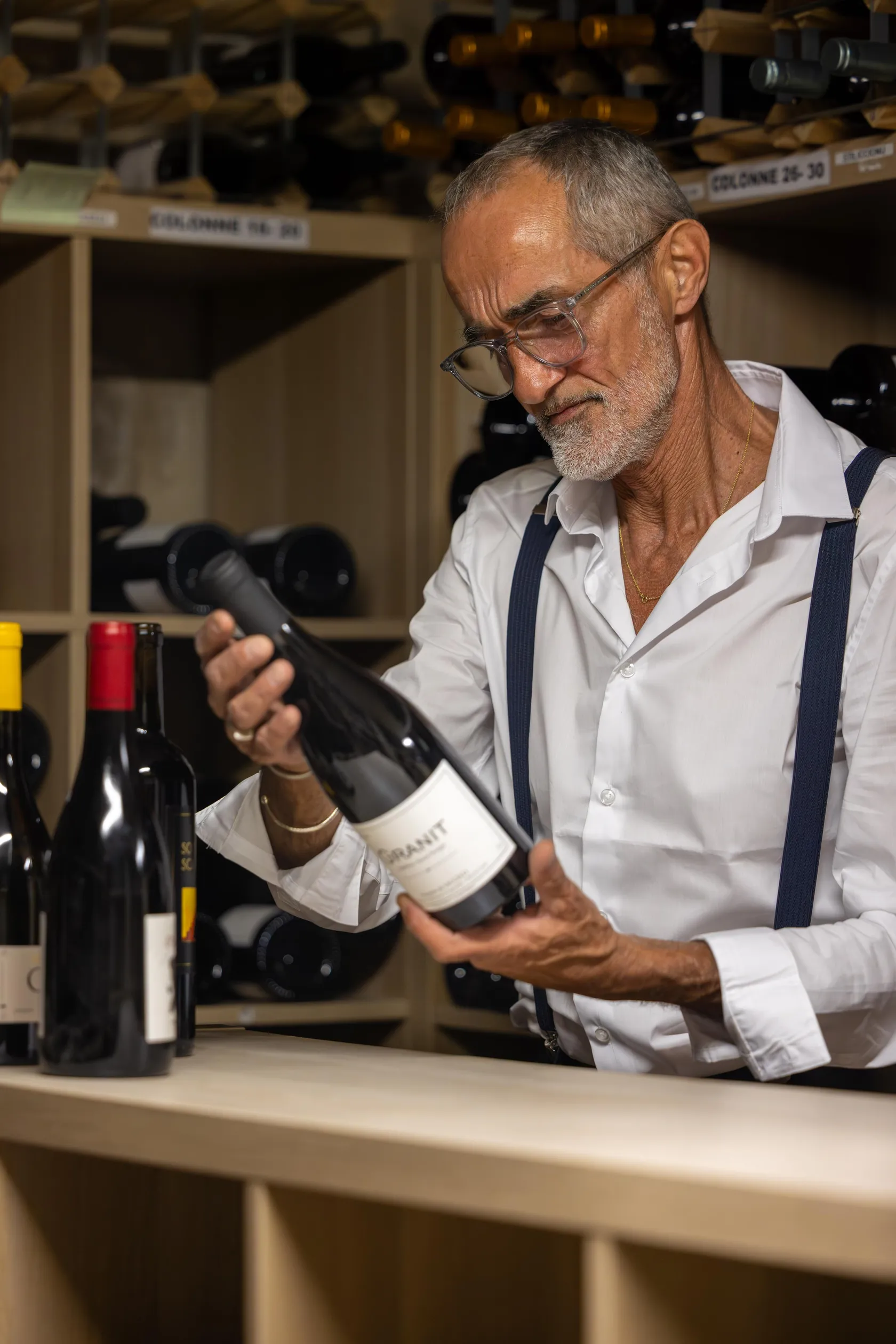 Un homme examine une bouteille de vin dans une cave à vin remplie de bouteilles.