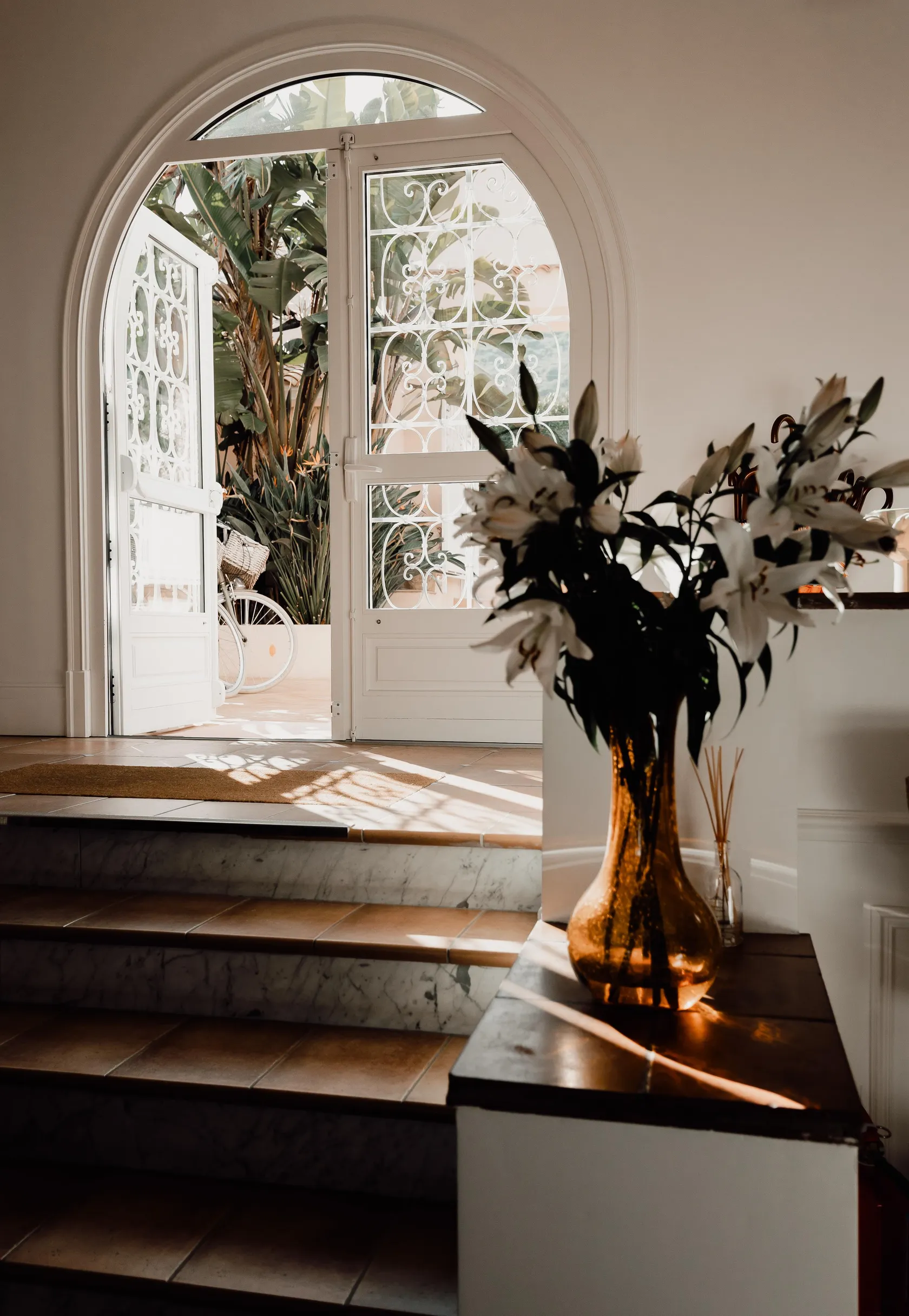 Eine Vase mit weißen Blumen steht auf einer Konsole nahe einer offenen Glastür, die Licht hereinlässt.