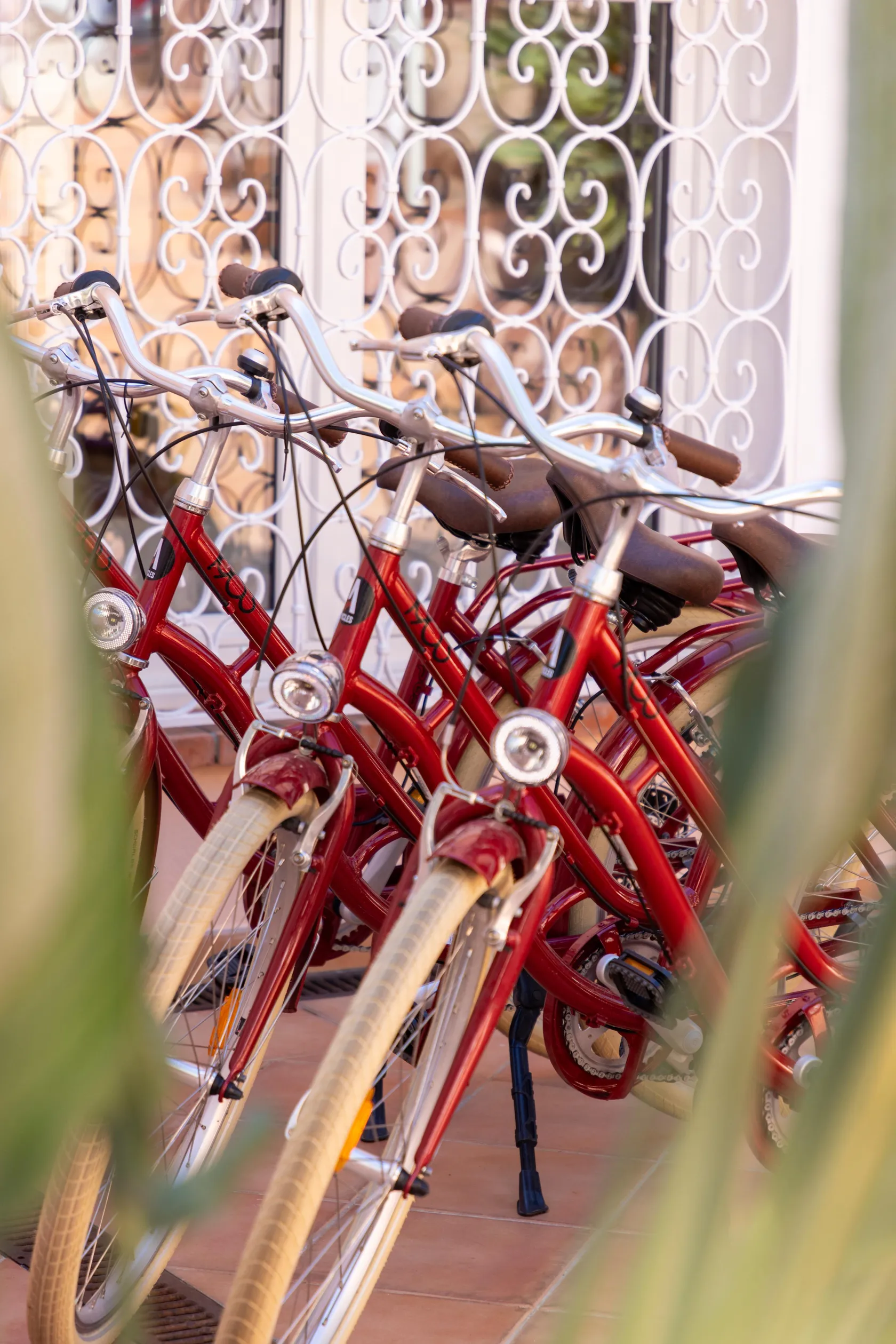Plusieurs vélos rouges sont alignés contre un mur orné d'un motif en fer forgé blanc
