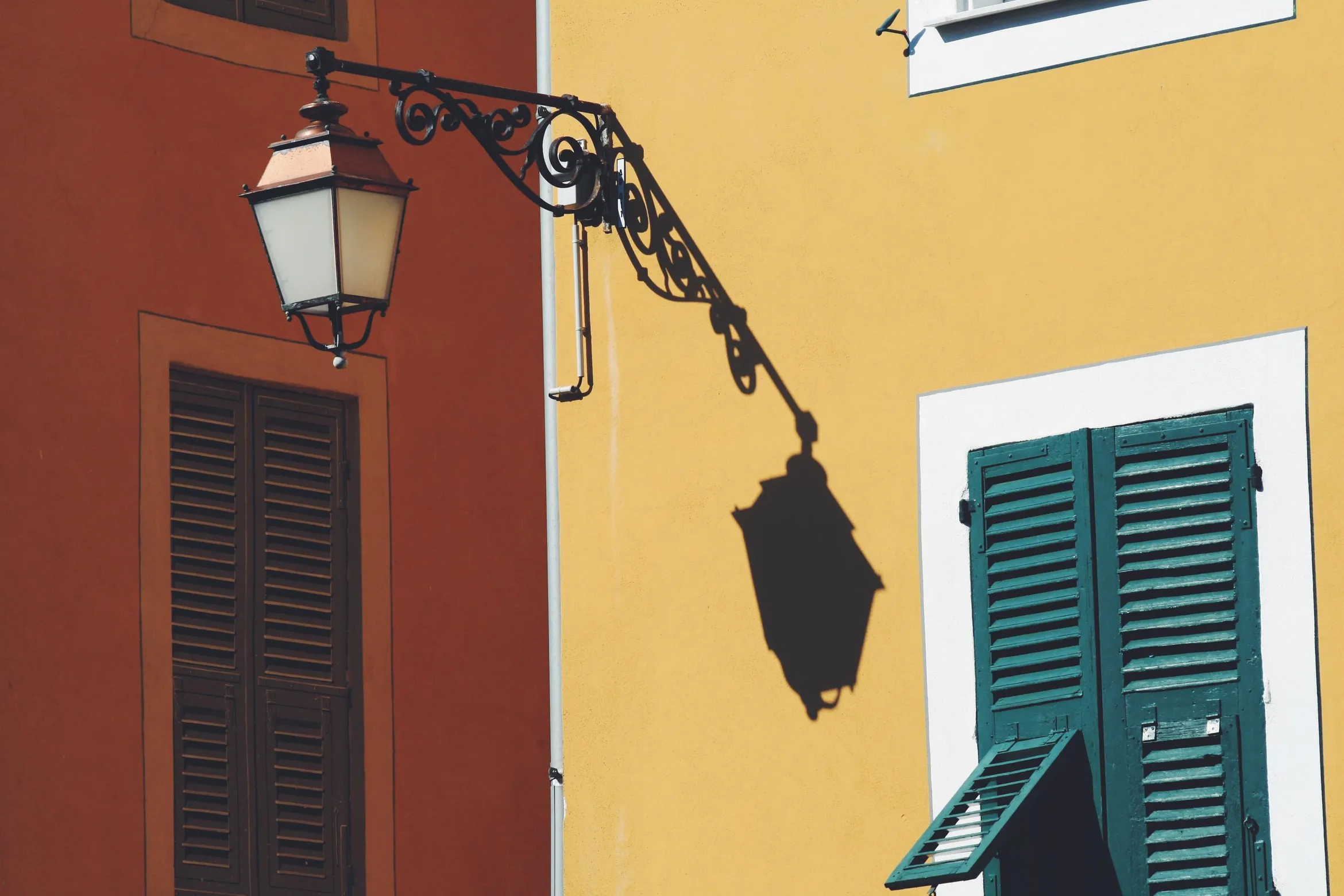 Wrought iron wall lamp fixed to a yellow wall with green and red shutters in the background