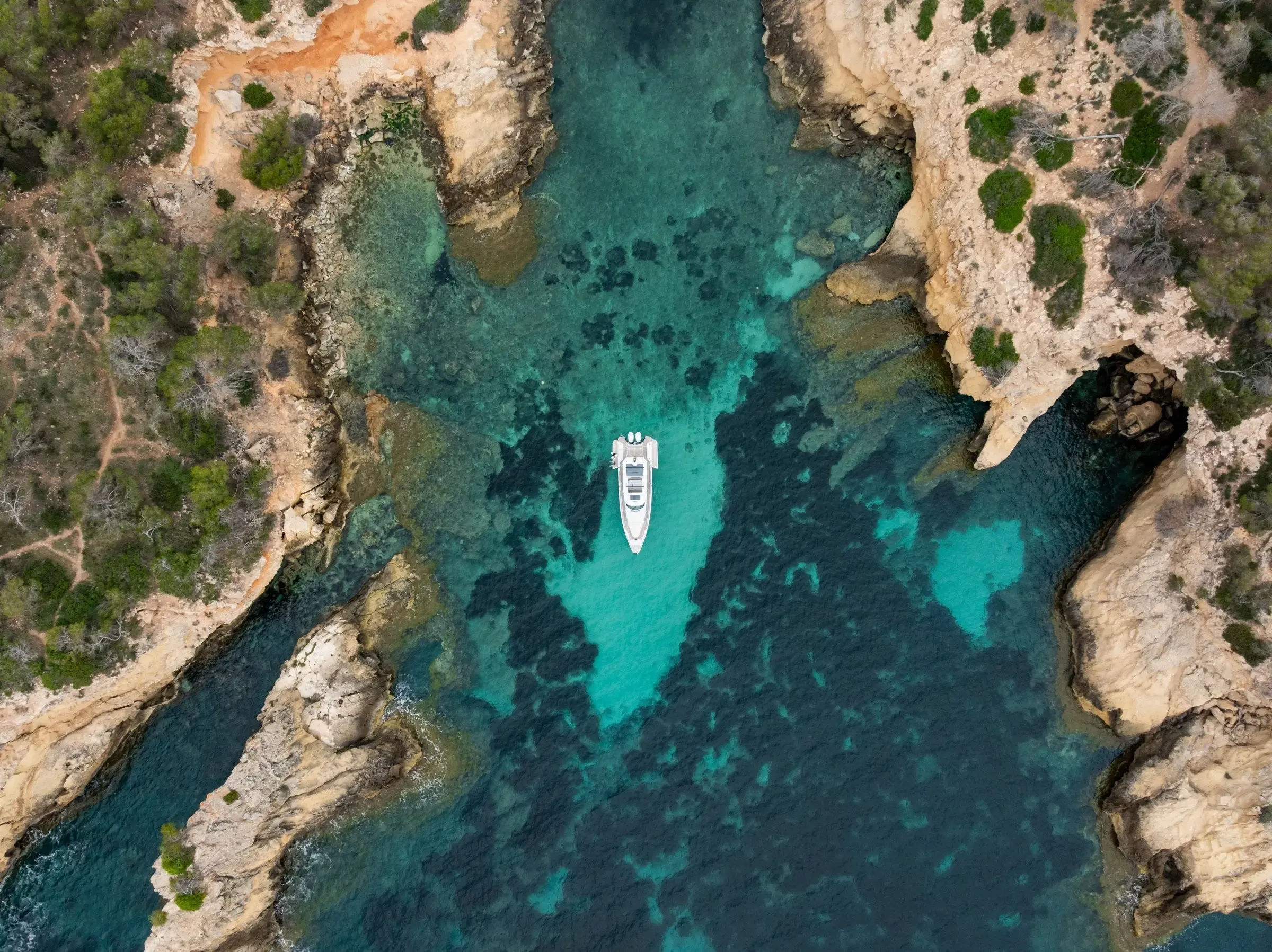 Un bateau blanc est ancré dans une crique entourée de rochers et d'eau turquoise
