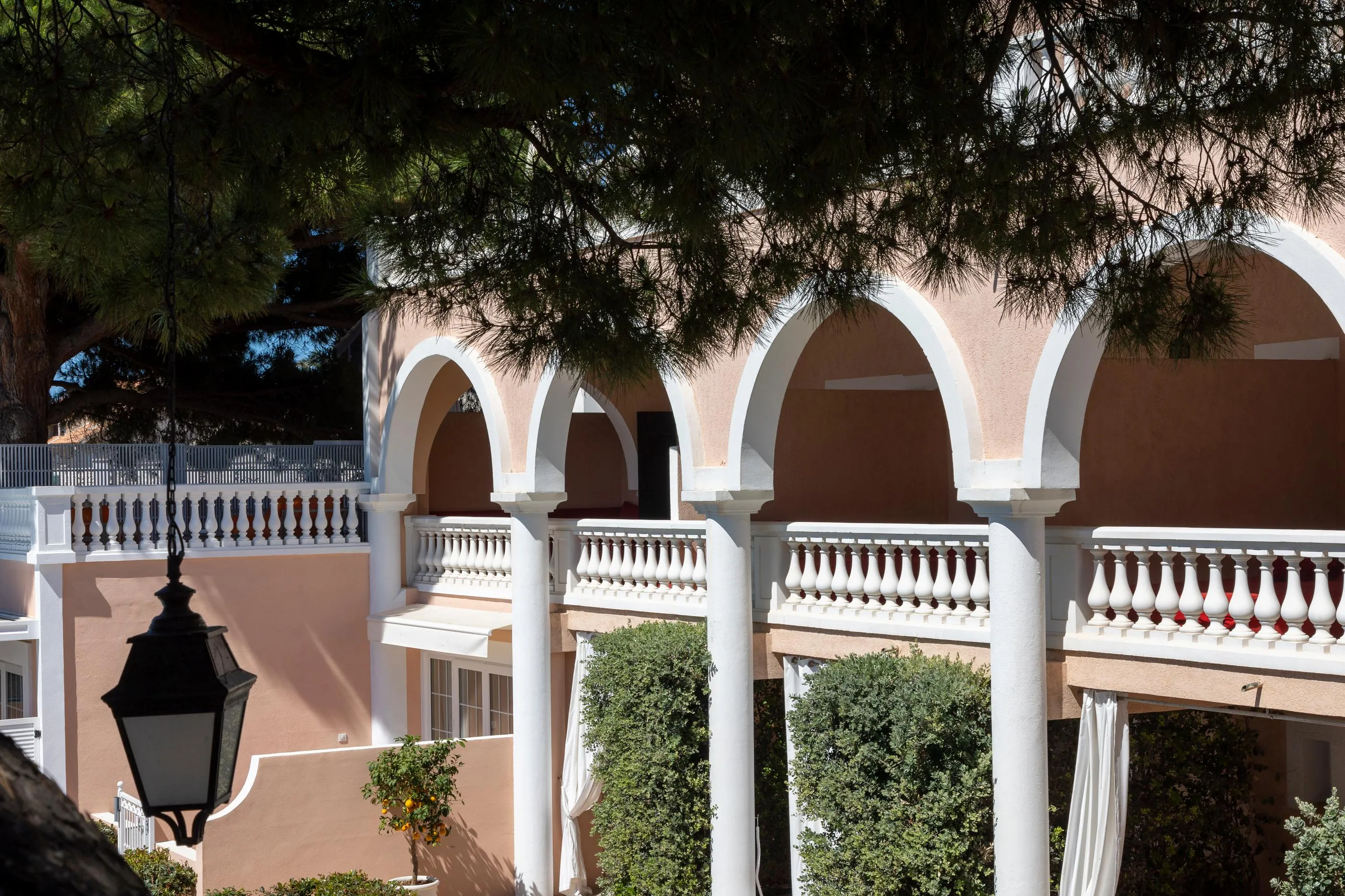 Balcon with arches and white balustrade, surrounded by trees and vegetation, with a black hanging lantern