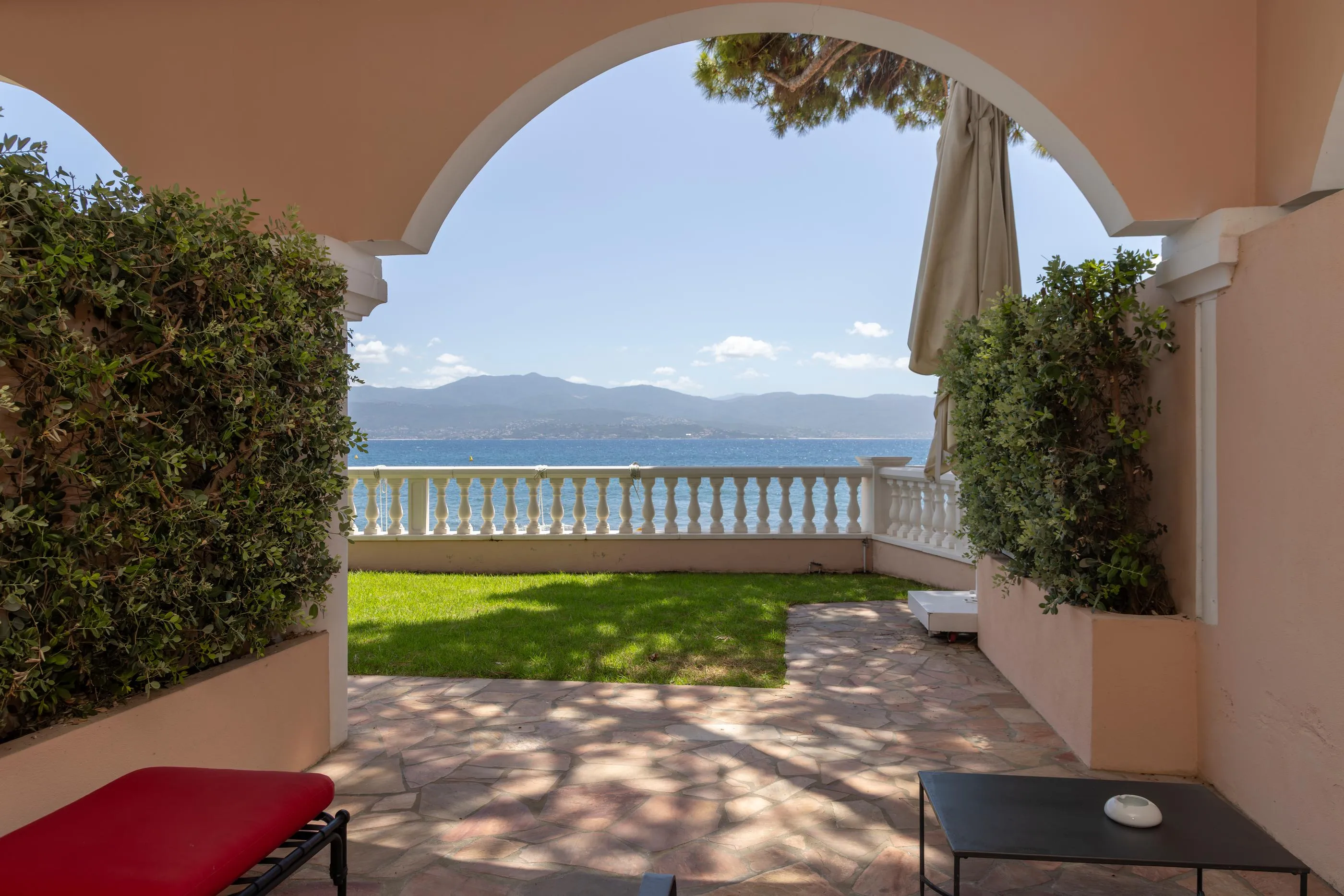Terrasse mit Meerblick und Bergblick, umgeben von Bögen und grünen Pflanzen, mit einem Tisch und einem Stuhl im Vordergrund