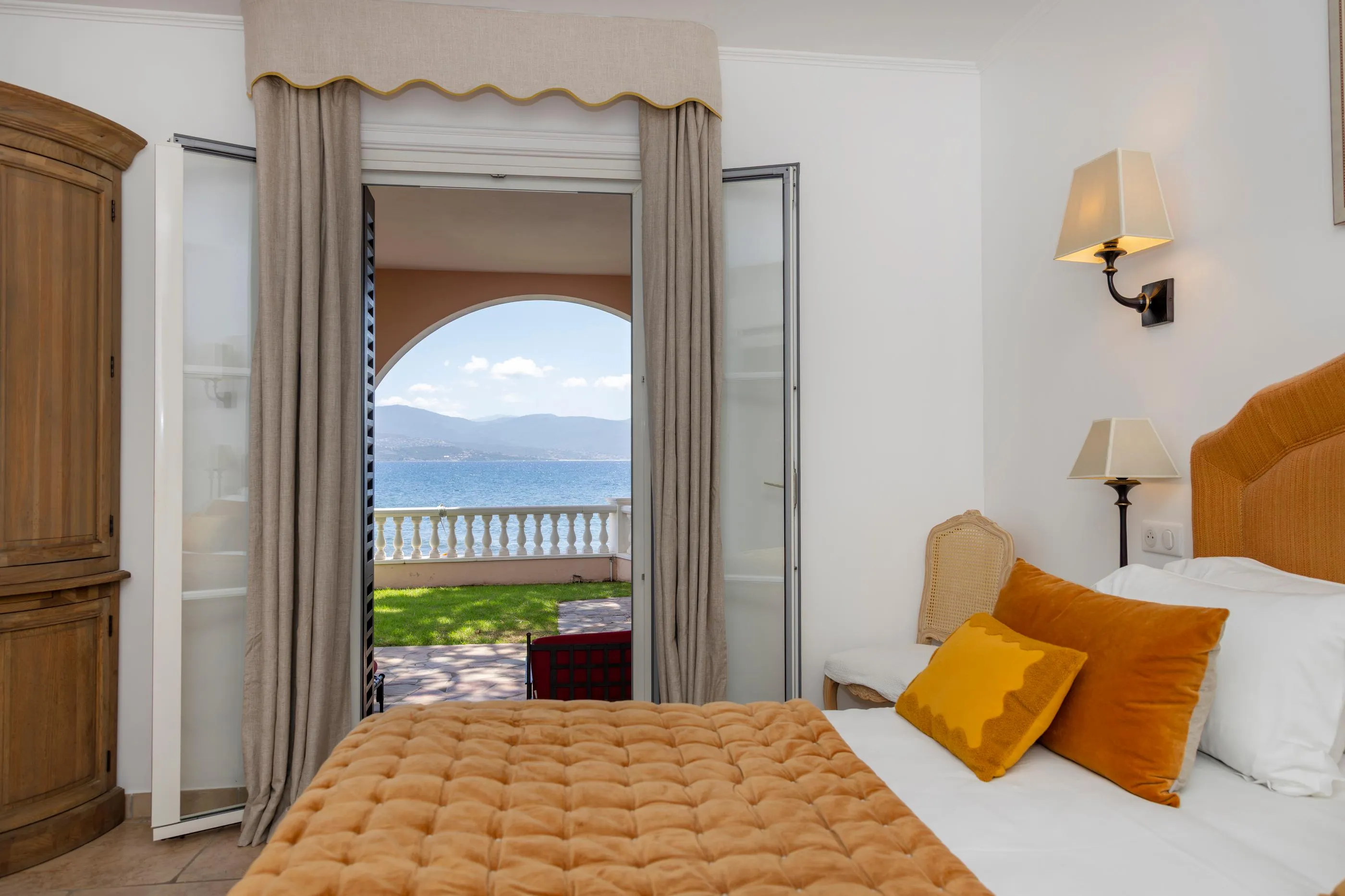 Chambre avec lit à tête en bois et vue sur un balcon donnant sur un lac et des montagnes