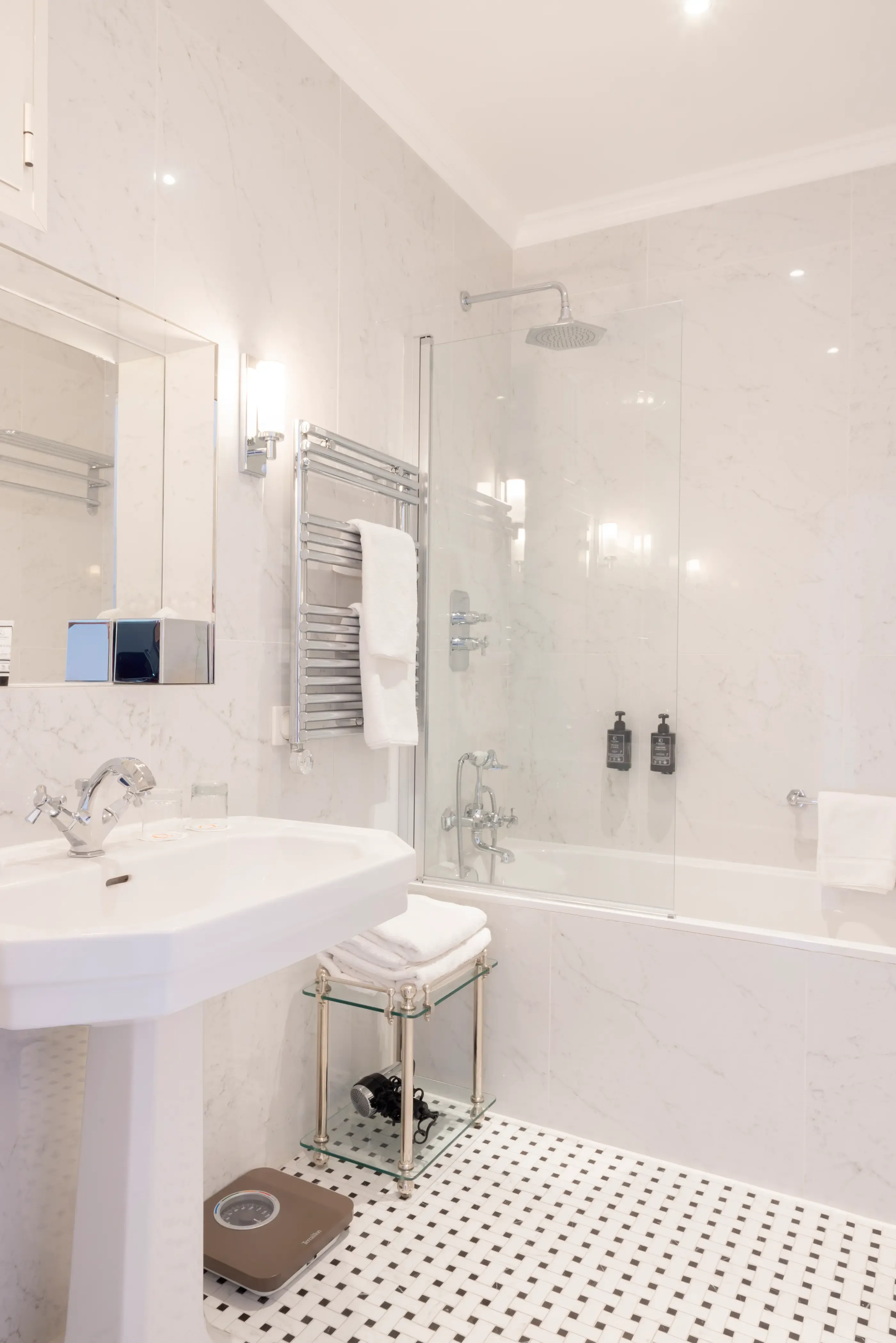 Modern bathroom with bathtub, rain shower, sink, mirror, towels, and black-and-white tiled floor