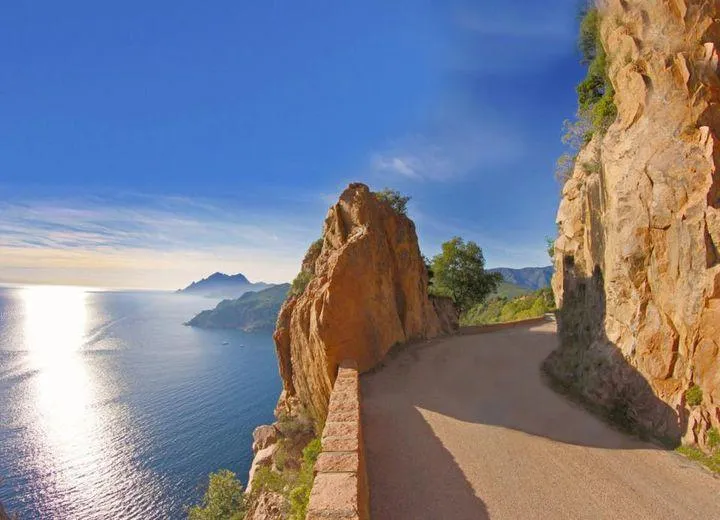Un chemin de terre longe une falaise rocheuse au-dessus d'une étendue d'eau bleue sous un ciel dégagé