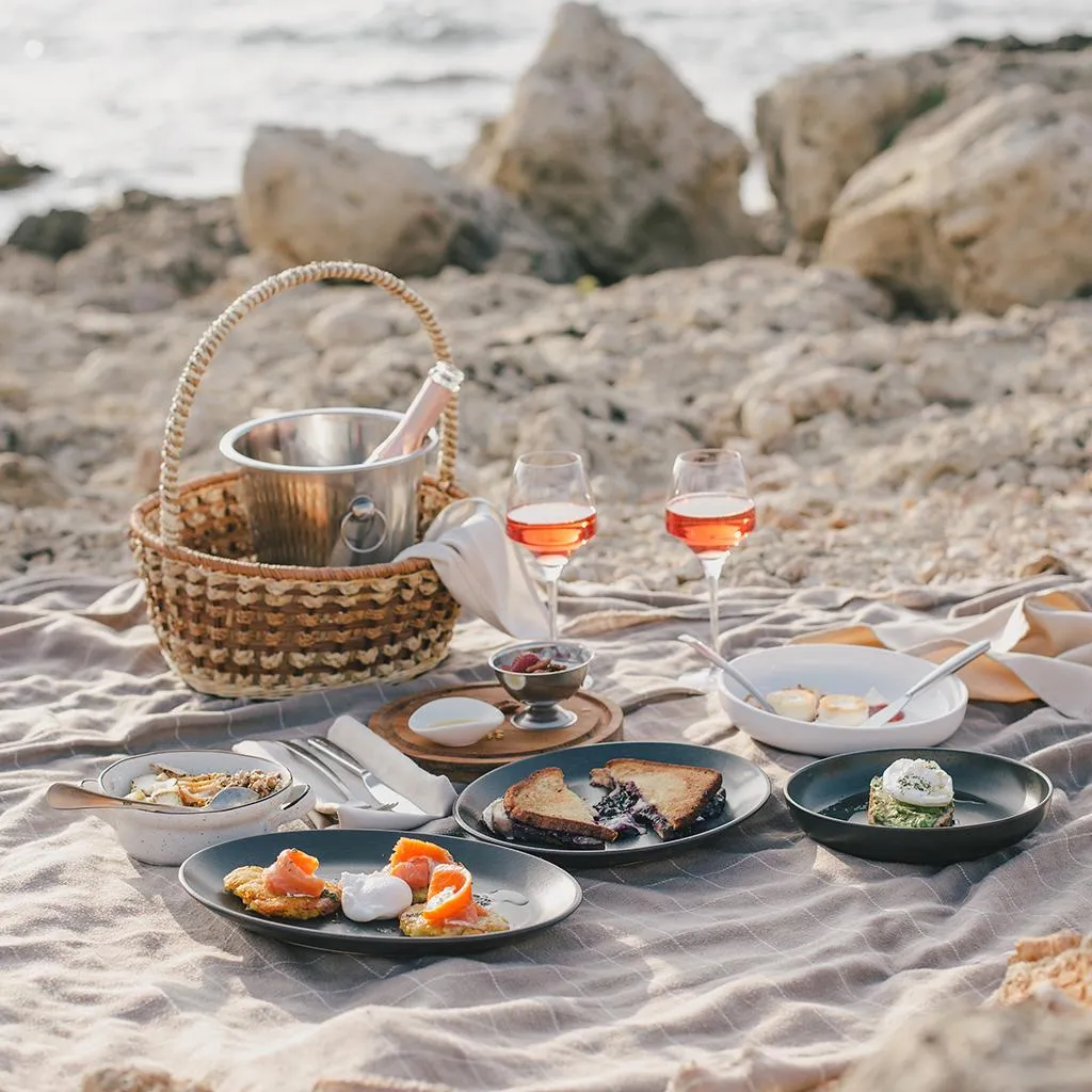 Un pique-nique avec des plats variés, des verres de vin et un panier à glace sur une couverture près de la mer