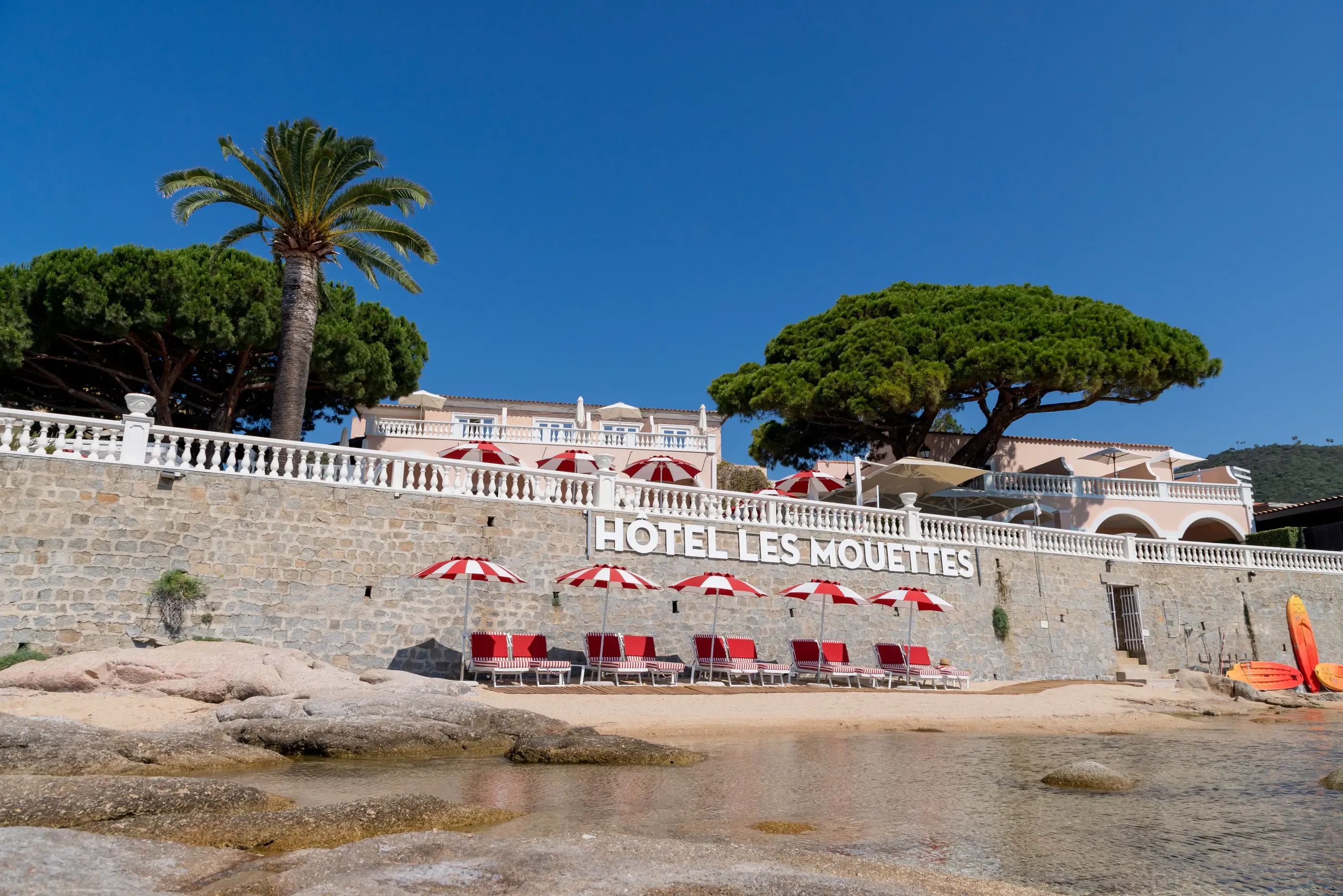 View of the beach in front of the Les Mouettes hotel, with red sun loungers and umbrellas lined up on the sand