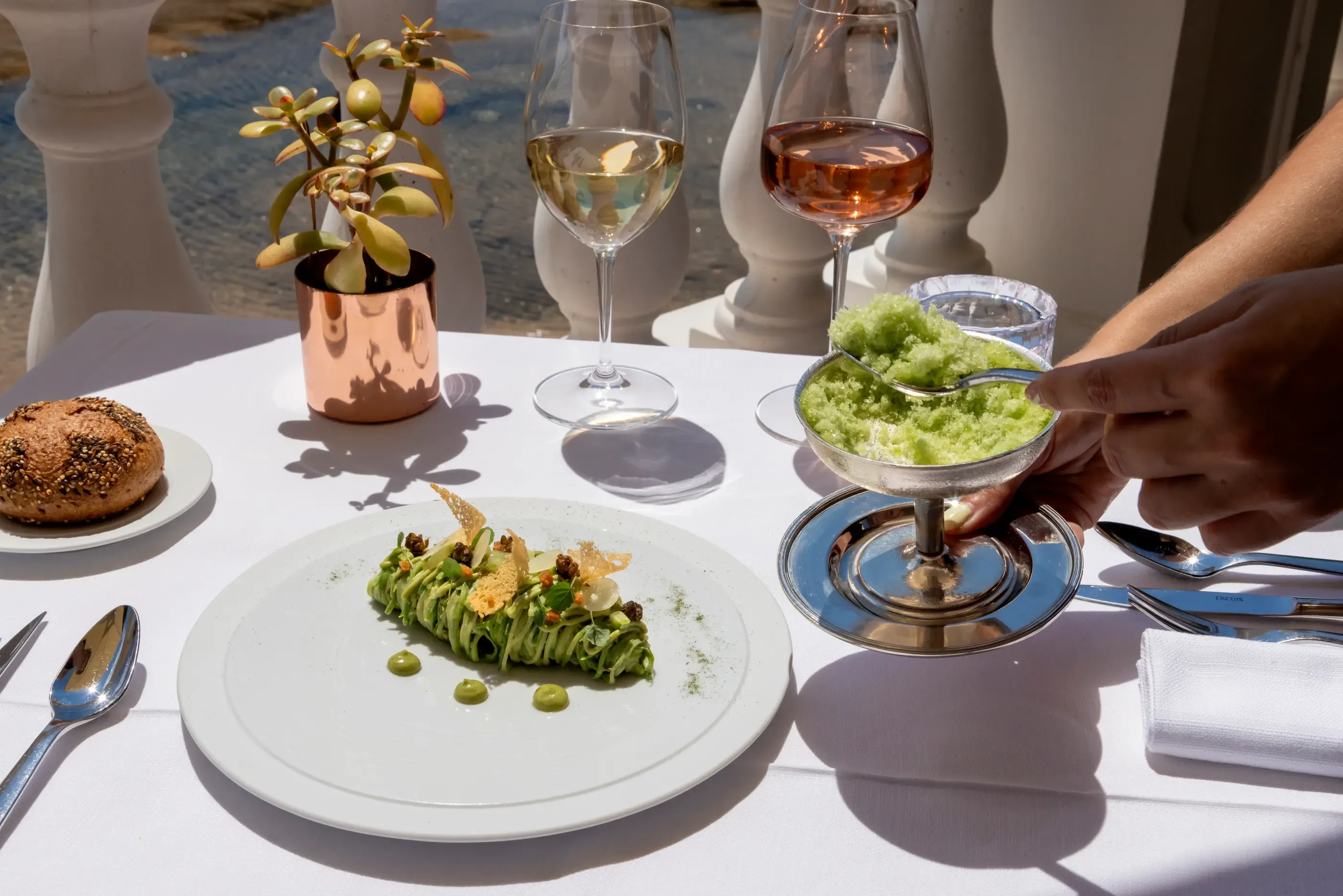 Une table avec des plats, des verres de vin et des couverts, en extérieur avec des personnes assises